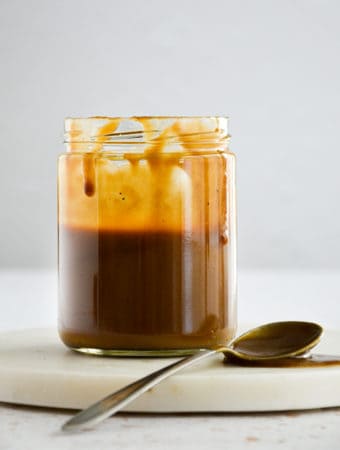 Vegan Salted Caramel in a mason jar with caramel dripping from the top and a spoon to the side with caramel on it