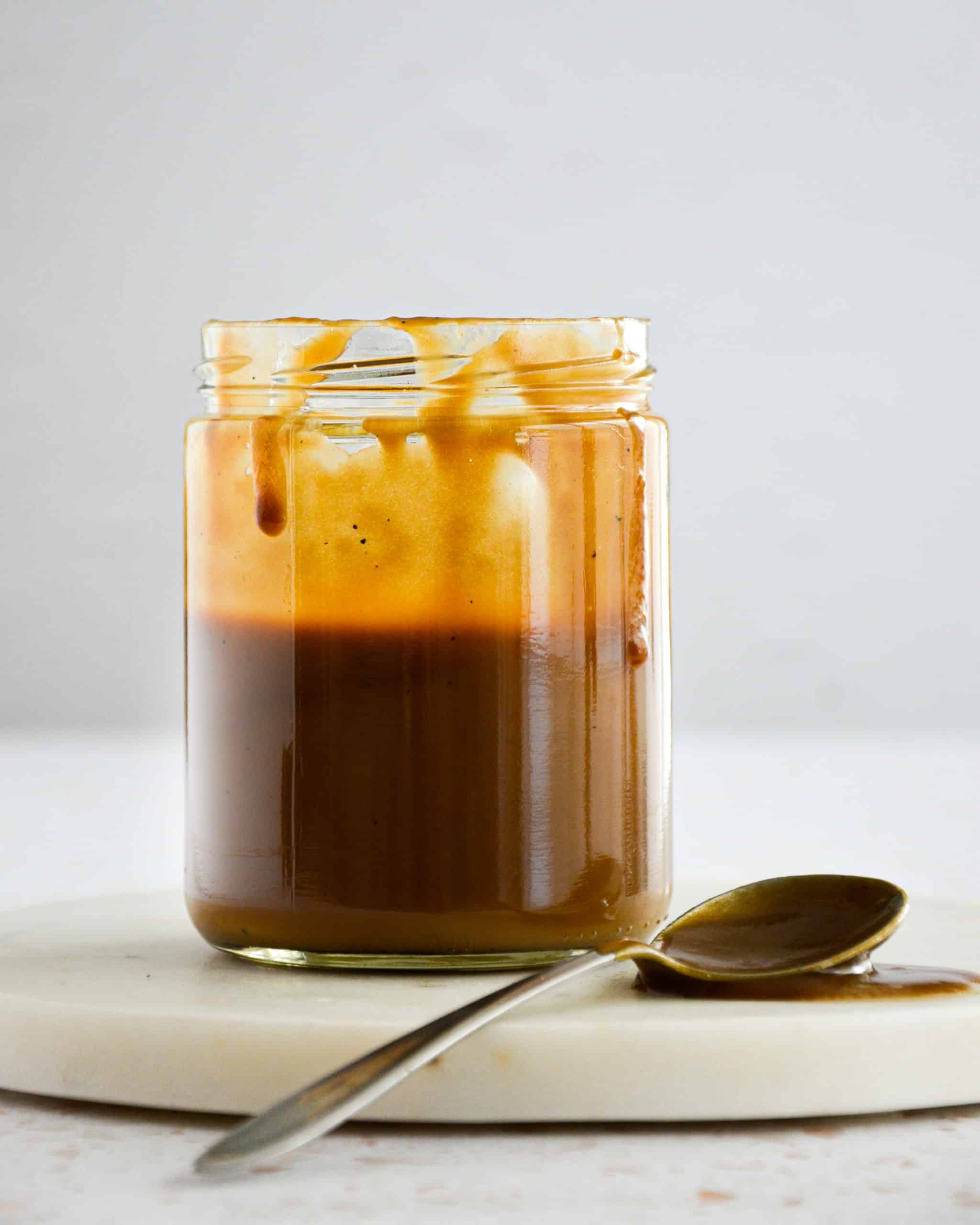 vegan salted caramel in a mason jar with caramel dripping off the sides. a spoon sits on the bottom.