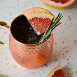 copper mug filled with a moscow mule and topped with two grapefruit wedges and rosemary sprig