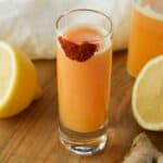 Featured square image of a lemon ginger cayenne shot with cayene powder on the rim and lemons in the background