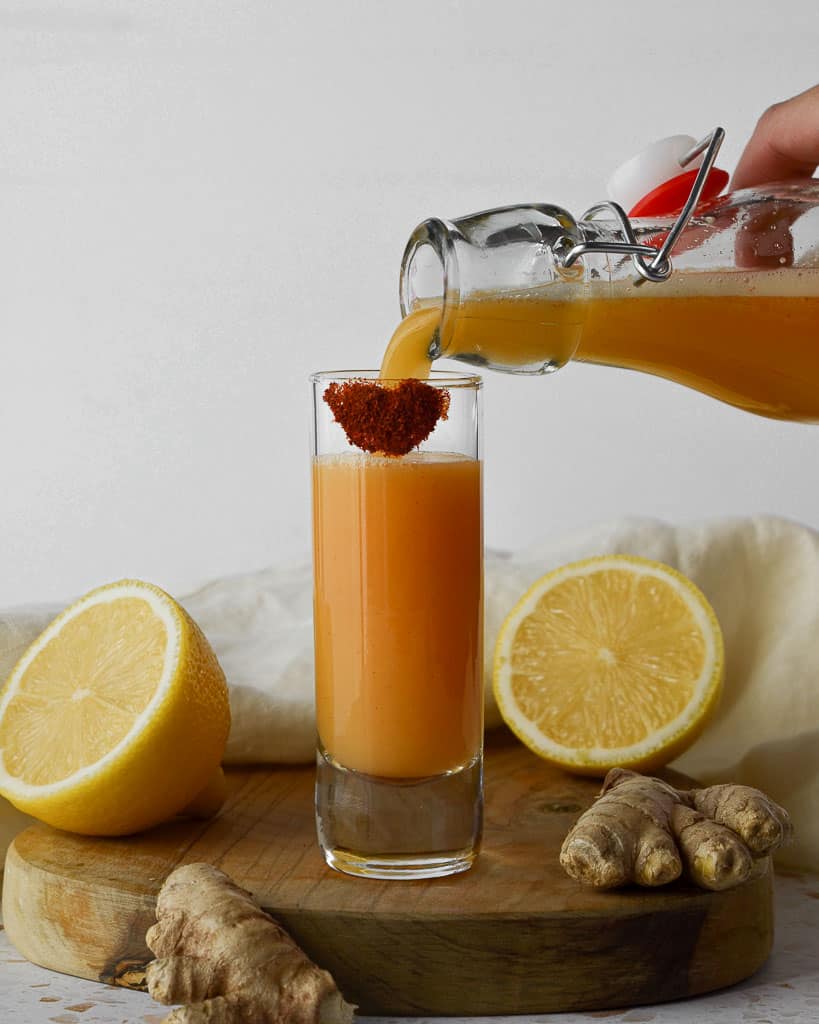 pour lemon ginger cayenne juice into a shot glass ready to drink