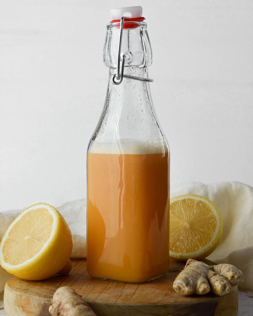 tall bottle of lemon ginger cayenne shots with lemon wedges in the background