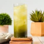 tall skinny glass with matcha gin fizz inside and two green plants in the back