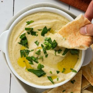 dipping pita bread into a creamy eggplant dip topped with parsley