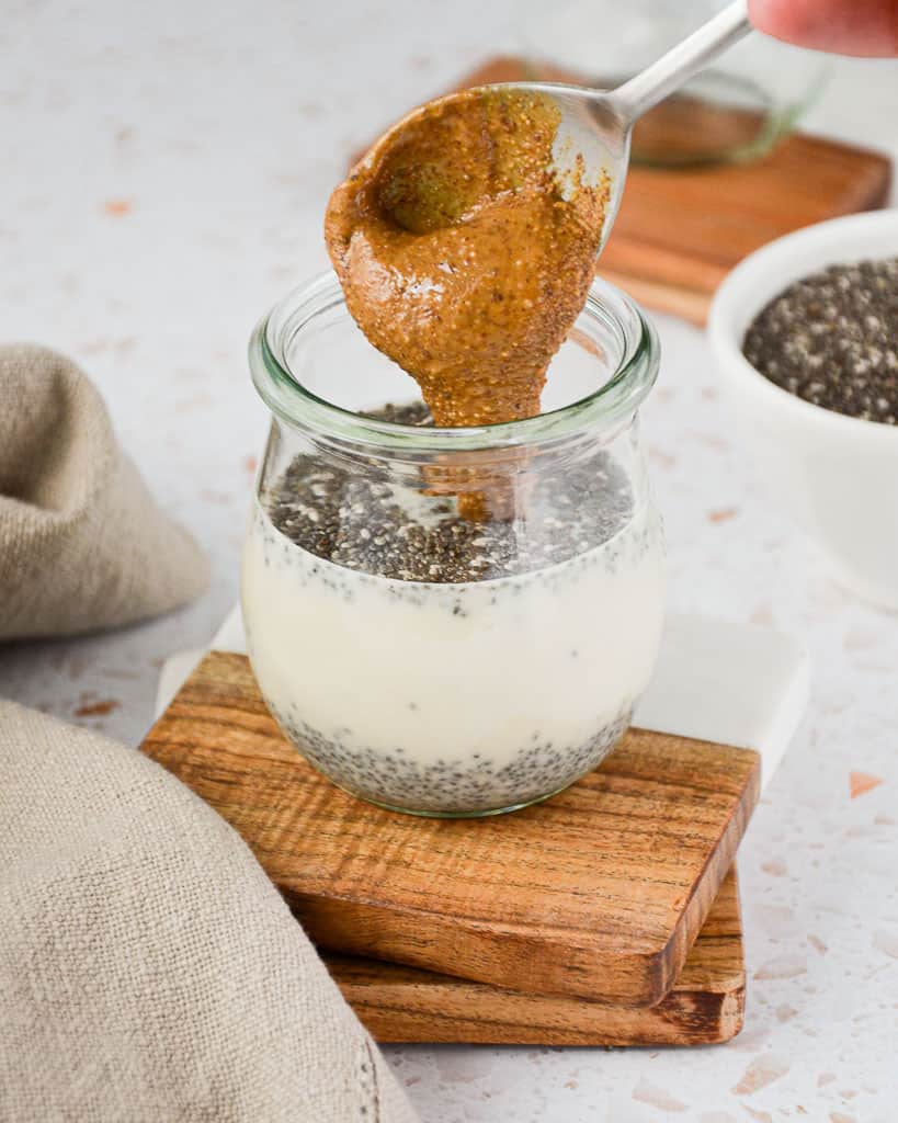 pouring peanut butter into a glass container filled with chia pudding