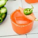 carrot juice margarita in a small glass topped with a carrot and a jalapeño slice