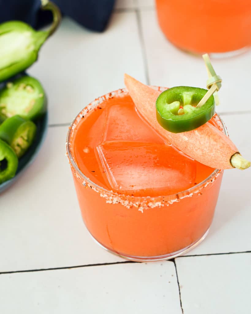 close up of a carrot juice spicy mezcal margarita and garnished with a jalapeño and baby carrot.