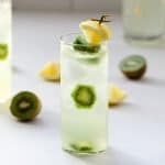 spiked vodka lemonade in a tall glass with a lime wedge and kiwis inside