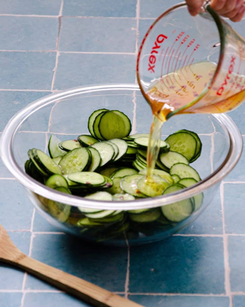 pouring marinade on thinly sliced cucumbers
