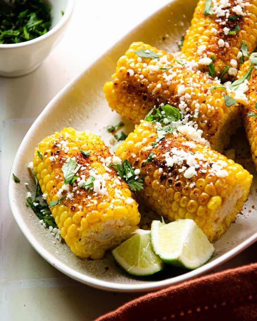 side view of mexican street corn on a plate with lime wedges