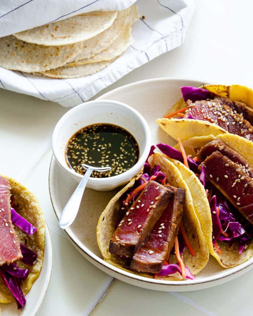 two plates of seared ahi tuna tacos with ponzu sauce and corn tortillas wrapped in a towel