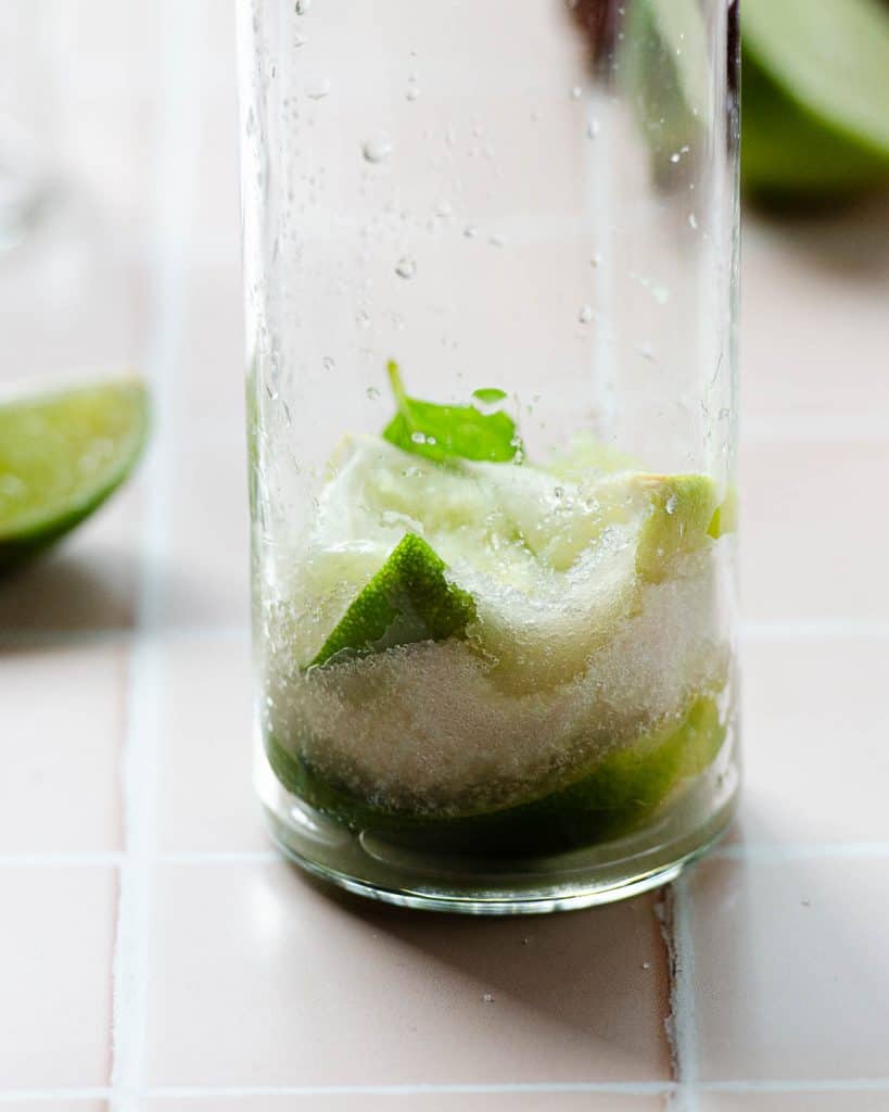 close up of muddled lime wedges, mint and sugar in a glass