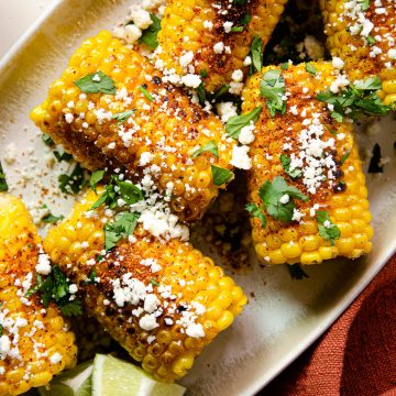 close up photo of corn on the cob with cotija cheese, cilantro and tajín