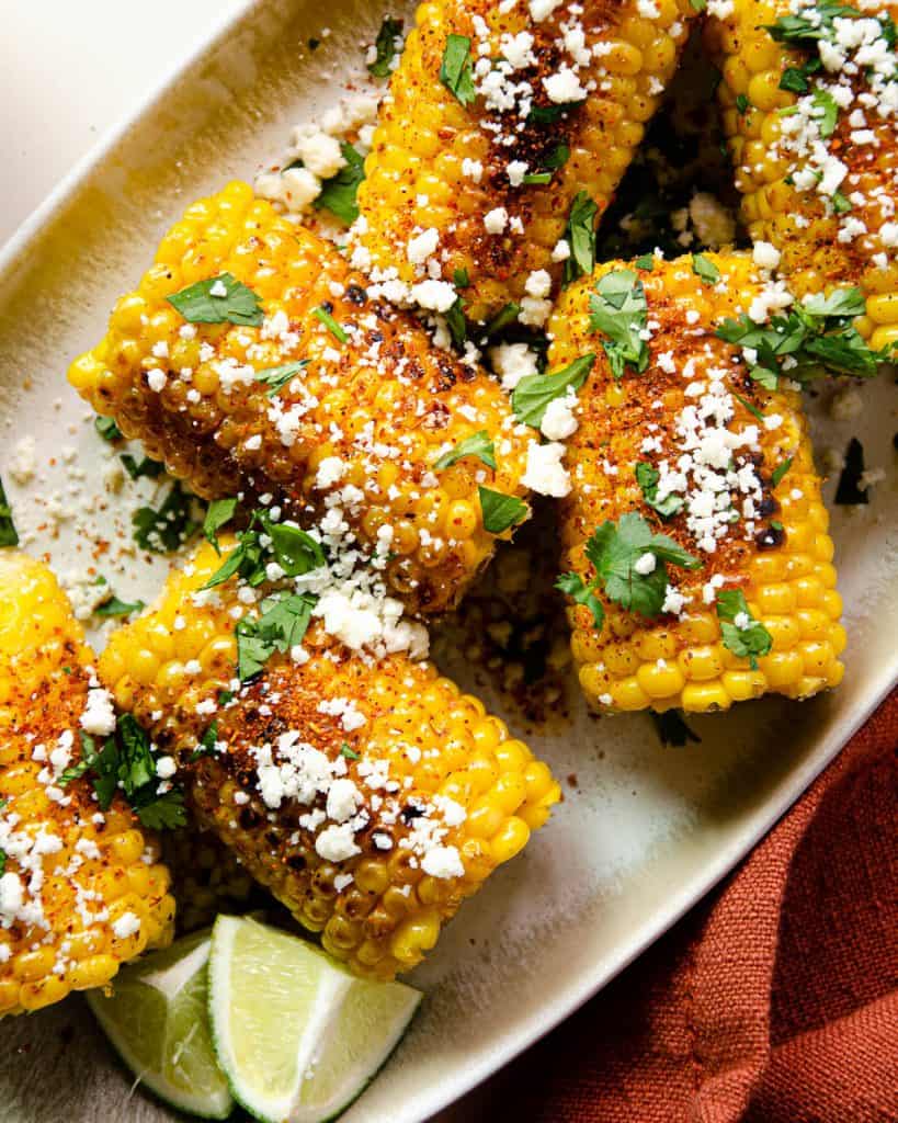 close up photo of corn on the cob with cotija cheese, cilantro and tajín