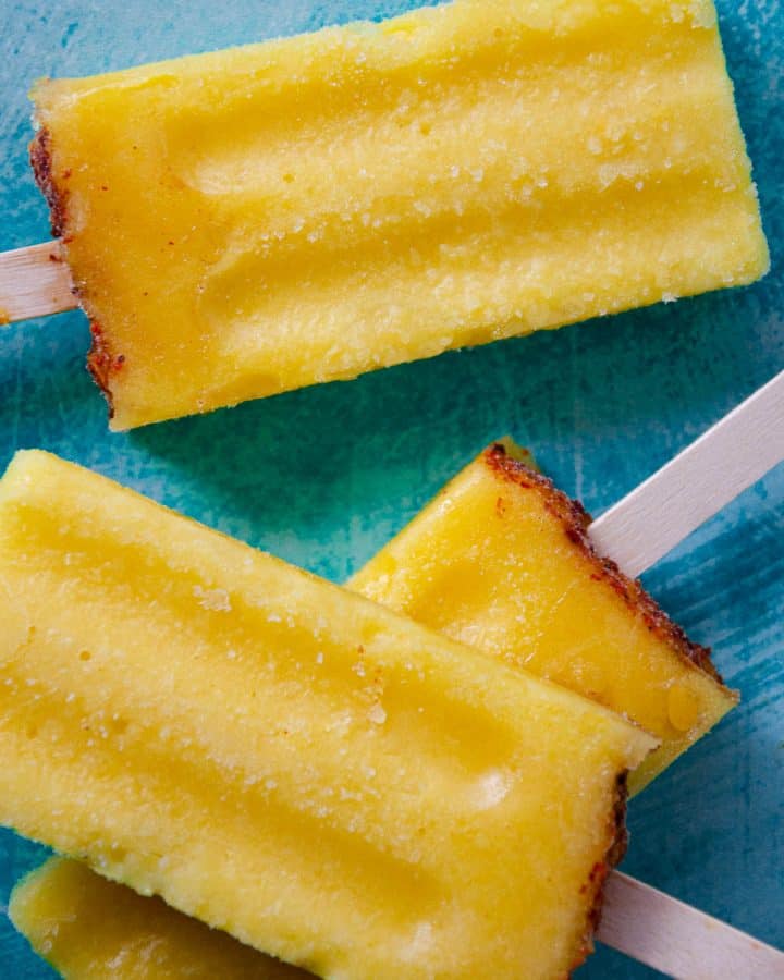 three yellow popsicles with a red tajin top layered on top of one another