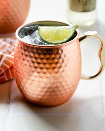 a copper mug filled with a mexican mule and garnishes with a lime wedge with another mexican mule in the background