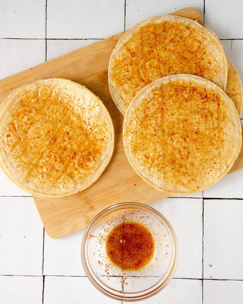 three corn tortillas with olive oil and tajin spread all over them on a cutting board