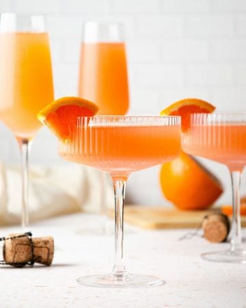 coupe glasses filled with blood orange mimosa and topped with orange slices and two tall champagne glasses