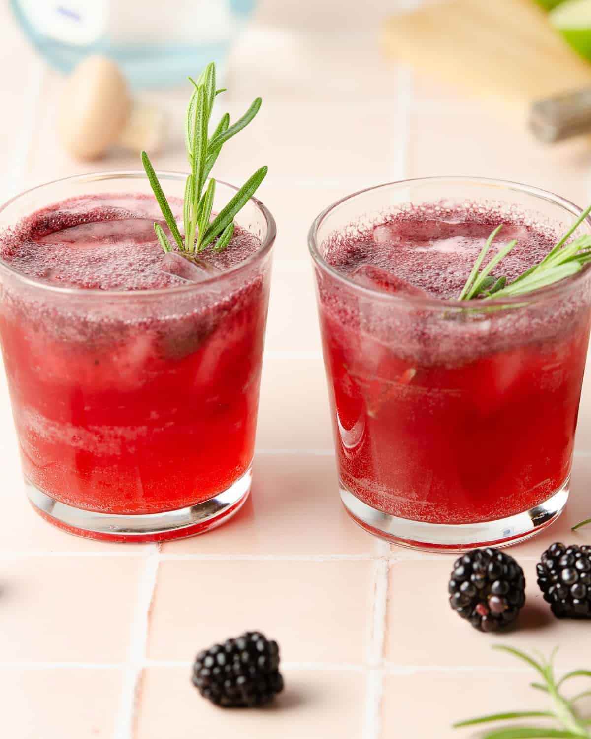 wo blackberry rosemary margaritas topped with rosemary sprigs and sparkling on top from the ginger beer