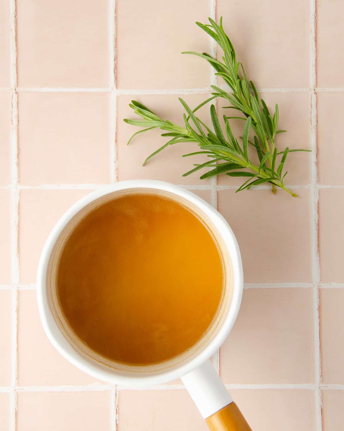 a pot of honey and water combined with rosemary leaves to the side, ready to make homemade rosemary syrup