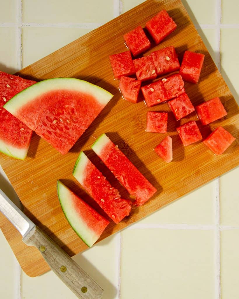 process shot of watermelon being cubed. First cut in half, then again to create cubes