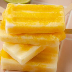 a square image of four mango popsicles on top of one another with a lime wedge in the back