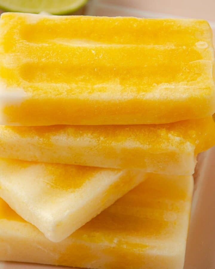 a square image of four mango popsicles on top of one another with a lime wedge in the back