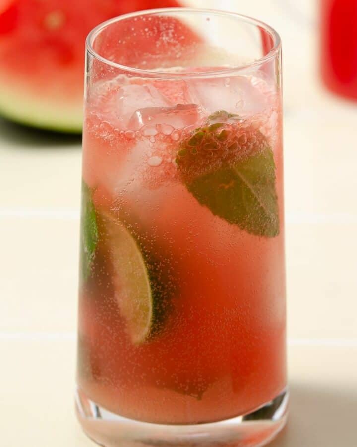 a square image of a pink watermelon gin mojito that is finished and filled with mint leaves and lime wedges
