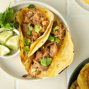 featured square image of beef barbacoa in a corn tortilla topped with fresh cilantro on a plate