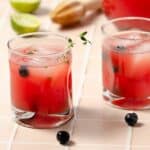 featured image square of two glasses of watermelon blueberry vodka smash in front with two stray blueberries. A large pitcher to the side with two fresh squeezed limes to the back left.