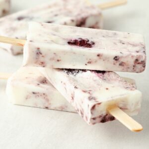 a square image of three blackberry popsicles stacked on top of each other with two additional popsicles laying to the side behind them