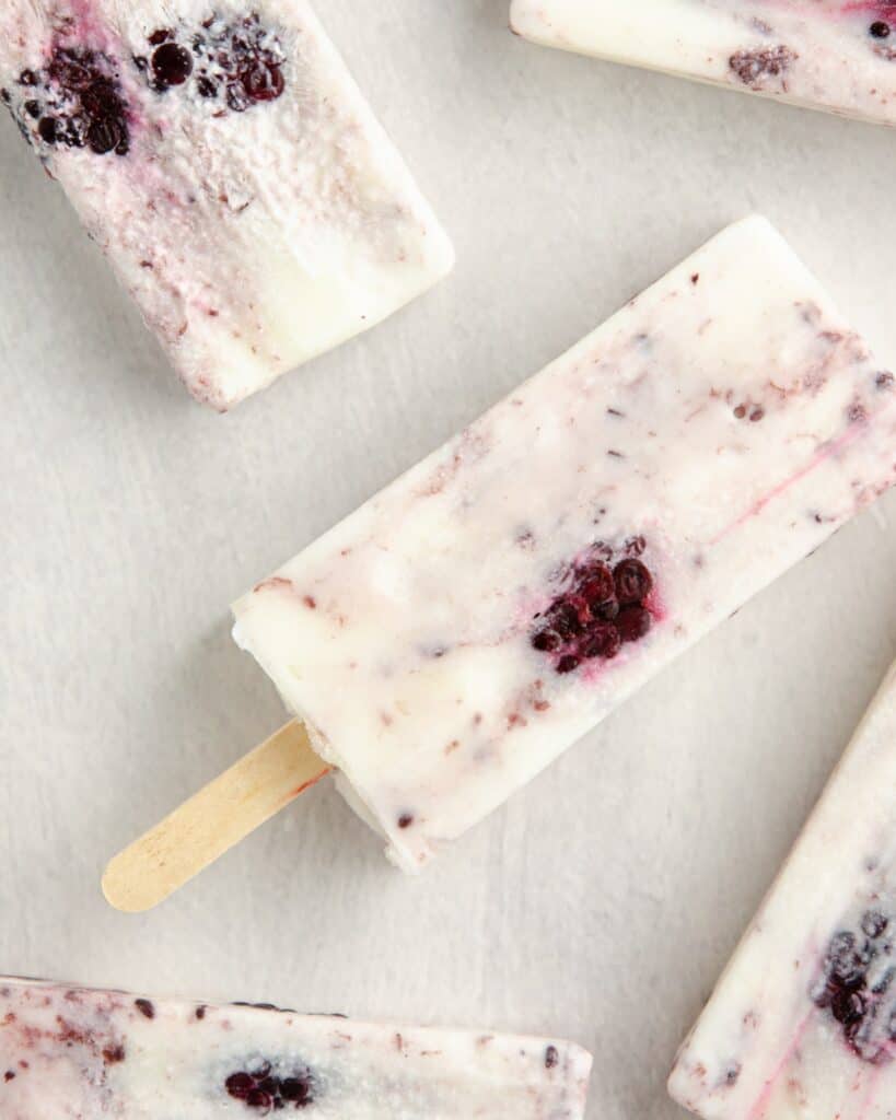 overhead shot of greek yogurt popsicles that are white with a reddish purple marble through and a blackberry peeping out
