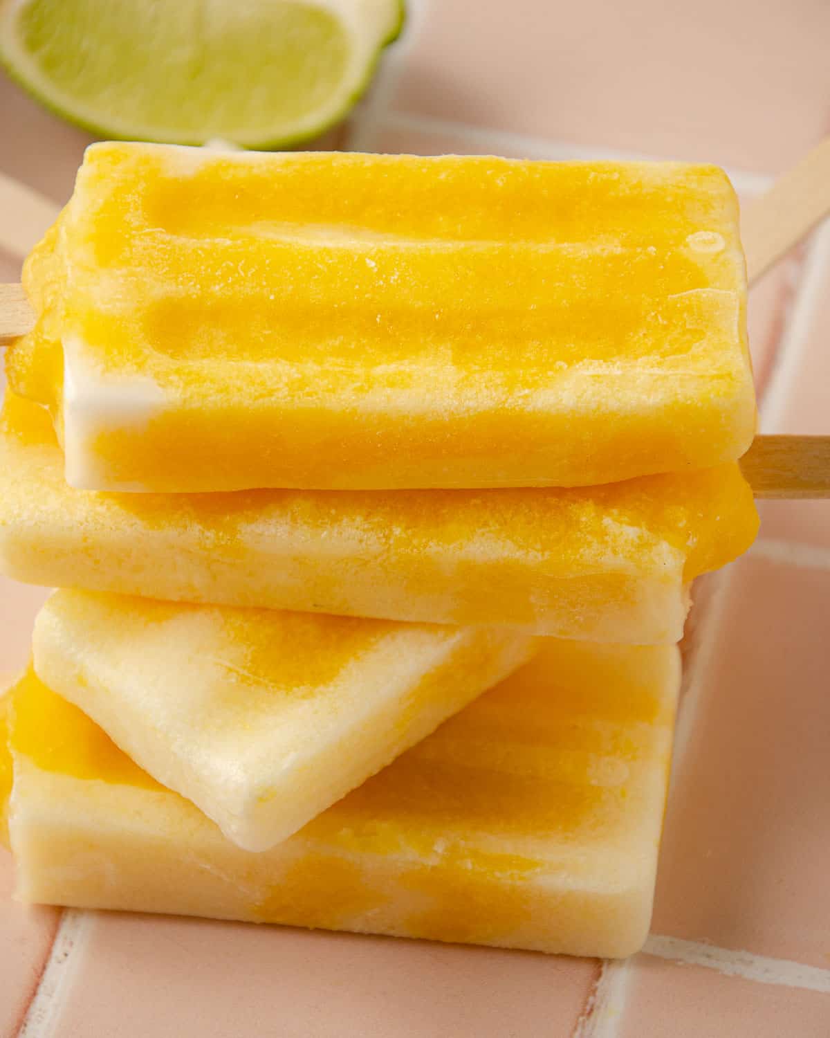 four mango popsicles on top of one another with a lime wedge in the back