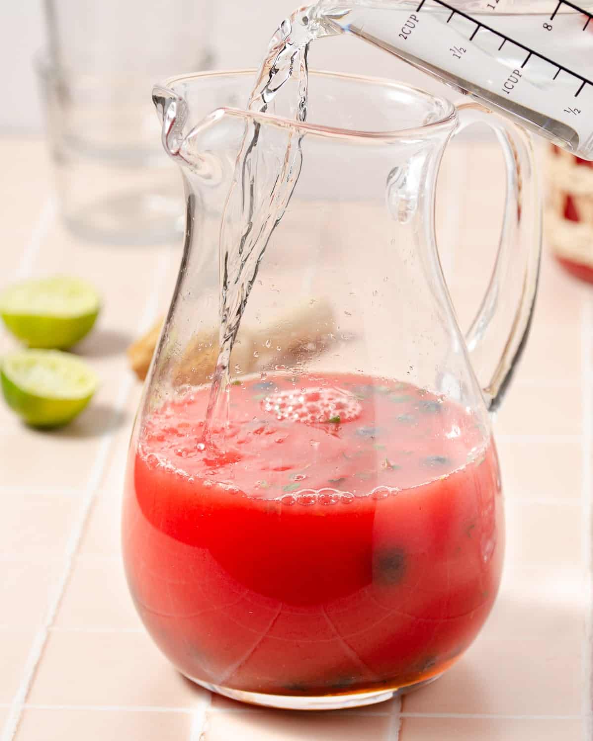 pouring vodka into a pitcher of watermelon juice blueberries and lime juice