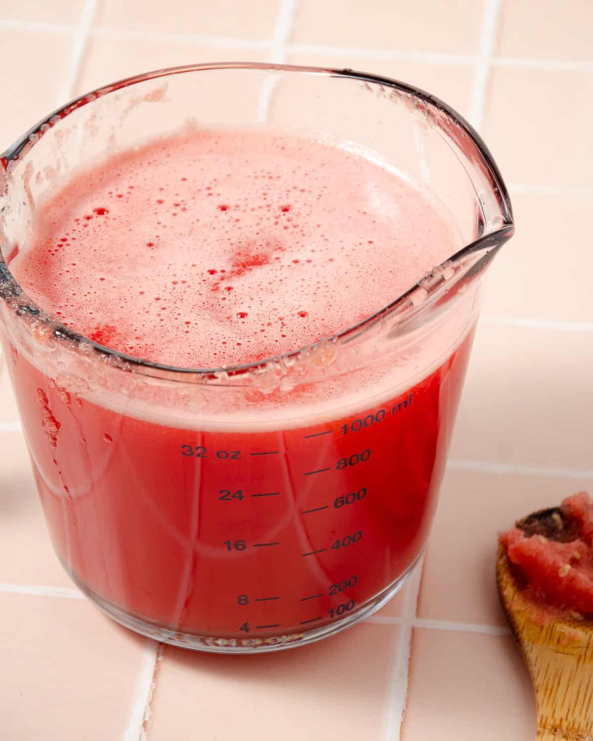 fresh watermelon juice in a measuring cup with a spoon with watermelon pulp to the side