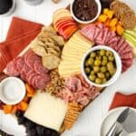featured image of a gluten free charcuterie board sit-in on a white wooden table with orange linens and a plate with cheese knives sitting to the bottom