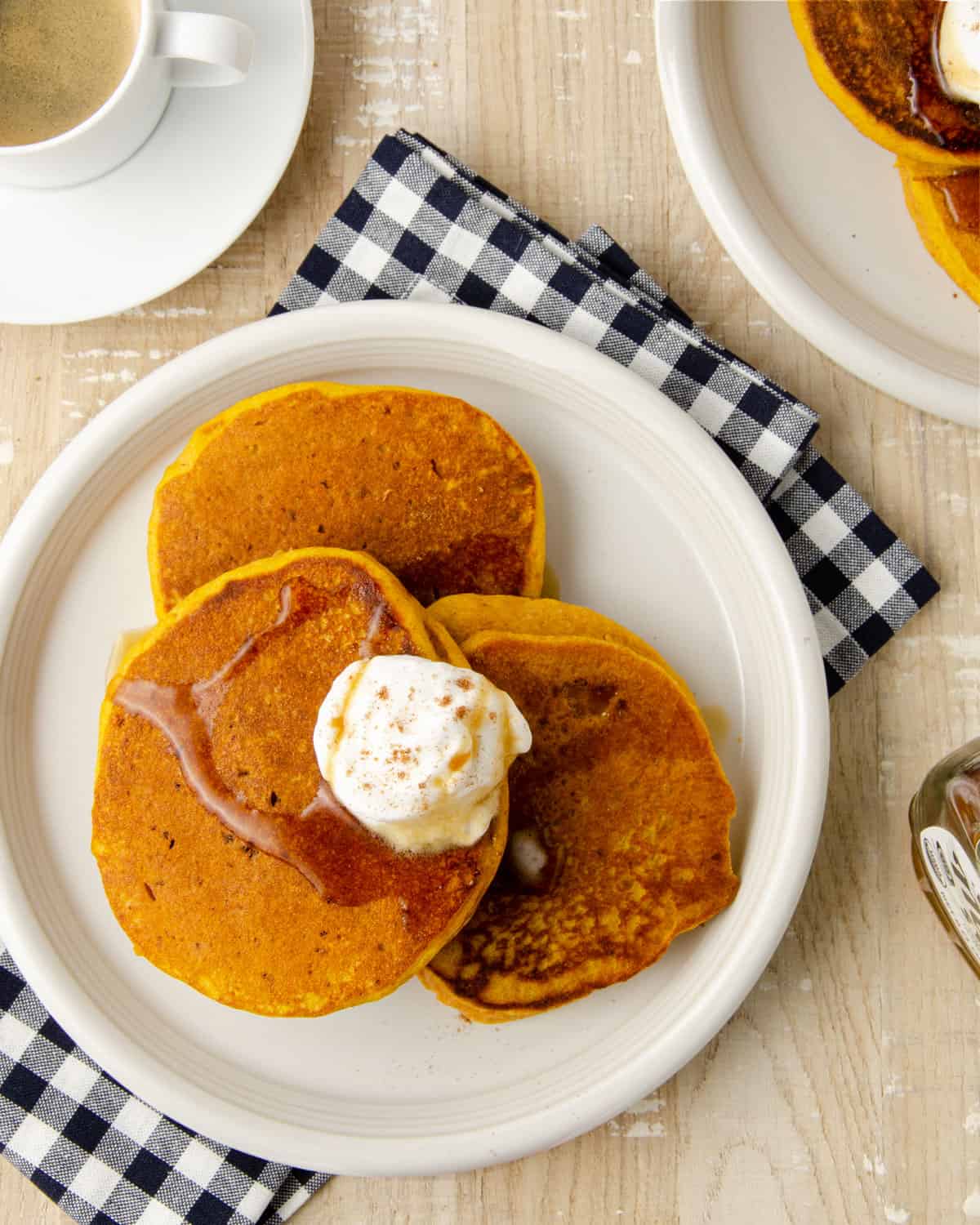 An overhead view of three pumpkin protein pancakes on a plate drizzled with maple syrup.