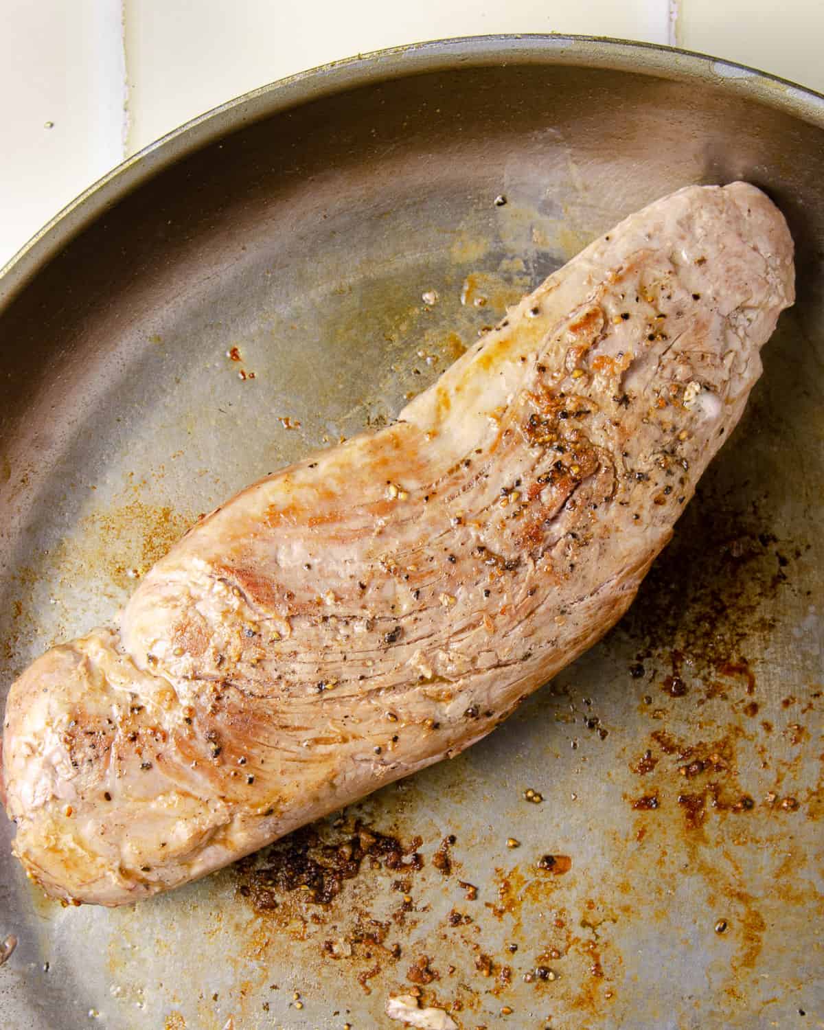 A seared pork tenderloin in a pan.