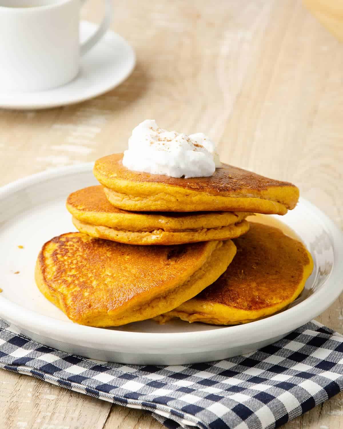 An angled view of four pumpkin protein pancakes on top of a plate.