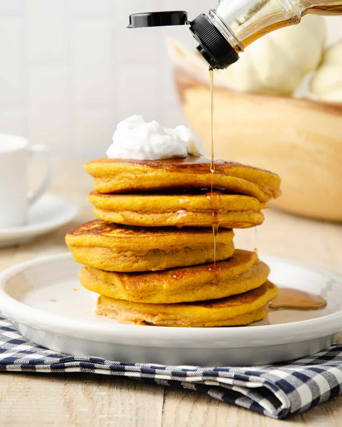 Pouring maple syrup on top of a stack of pancakes.