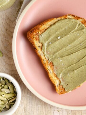 Pumpkin seed butter spread on a piece of toast on a pink plate.