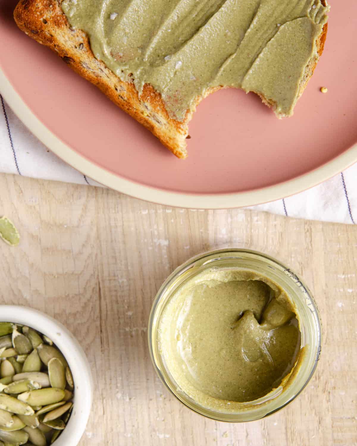 A bite out of a toast with pumpkin seed butter spread on top.