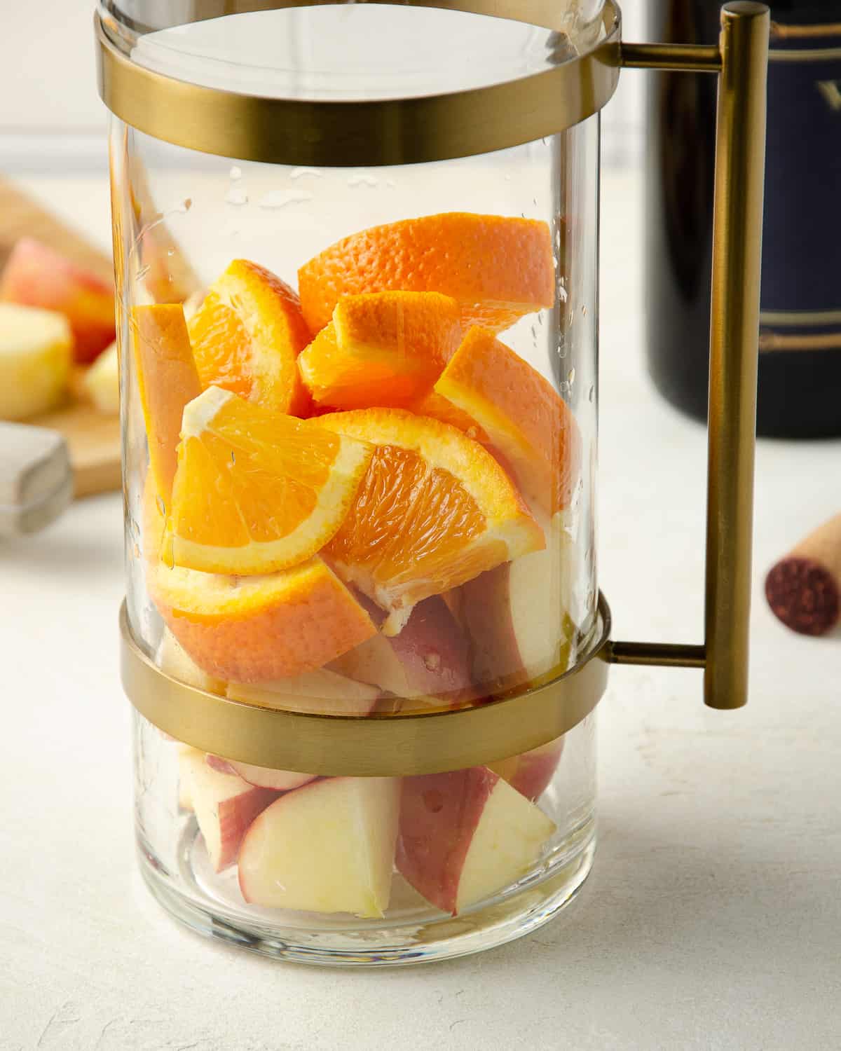 A pitcher filled with cut oranges and apples.