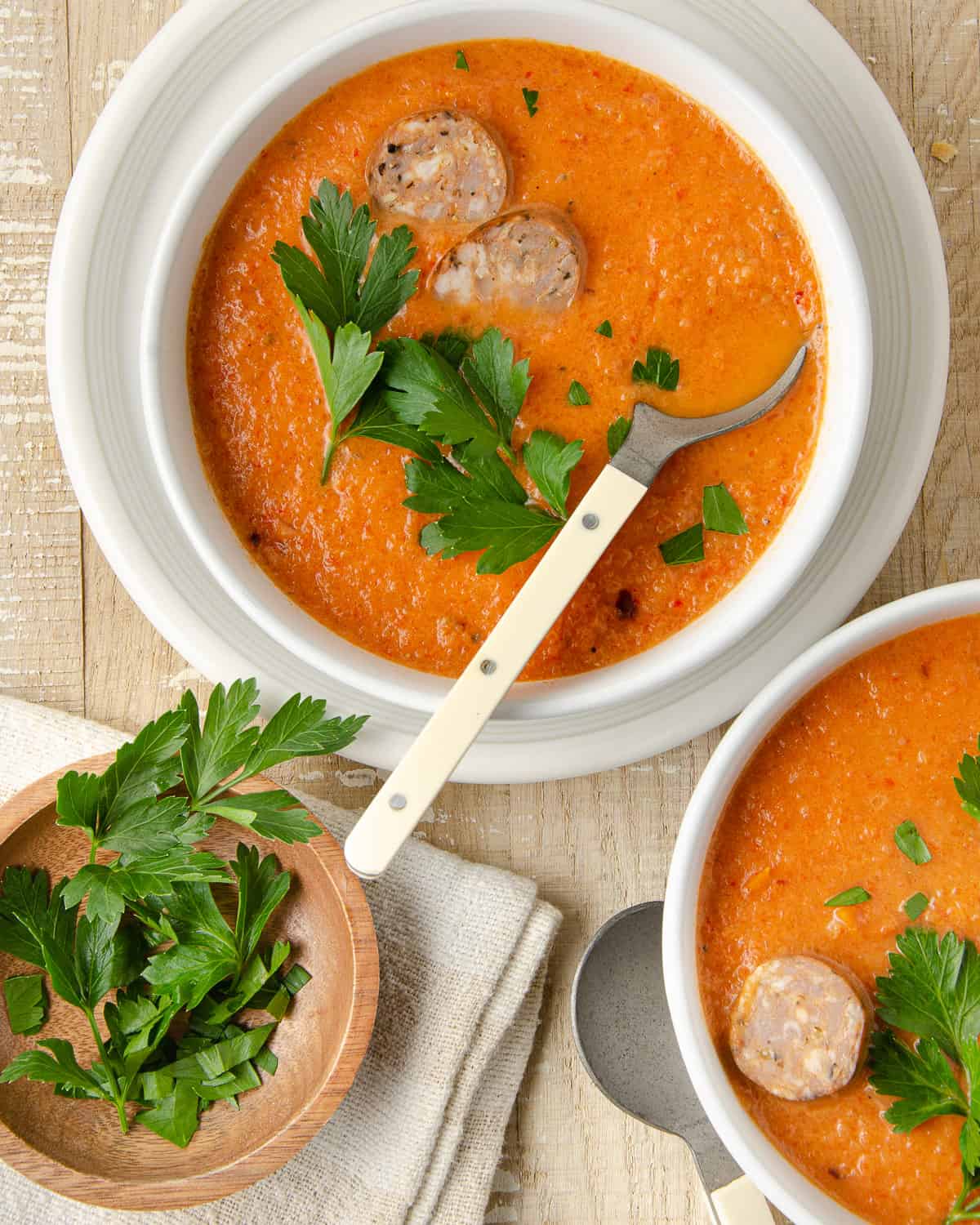 Two bowls of red pepper sausage soup topped with parsley.