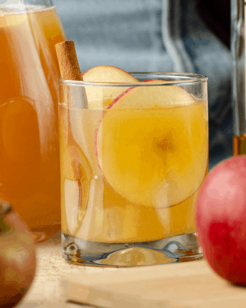 Close up of a spiked apple cider cocktail with a cinnamon stick and apples.