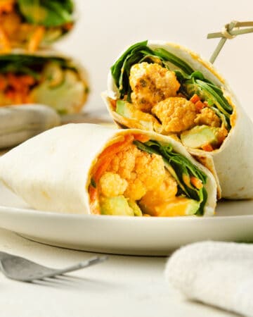 A close up view of a wrap split in half, able to see the roasted cauliflower.
