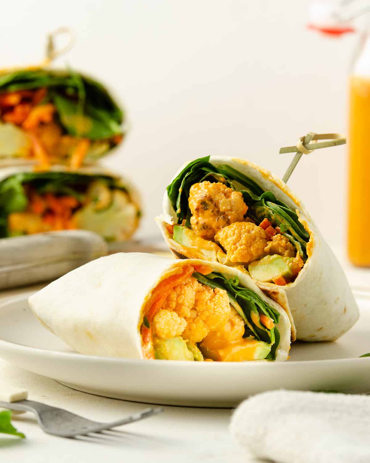 An angled view of two vegan wraps cut in half on top of a plate.