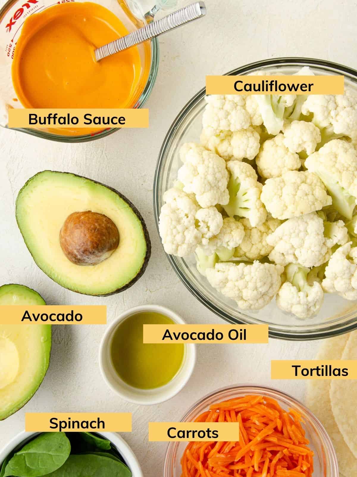 Ingredients to make a vegan wrap: cauliflower, tortilla, carrot, spinach, avocado and buffalo sauce.