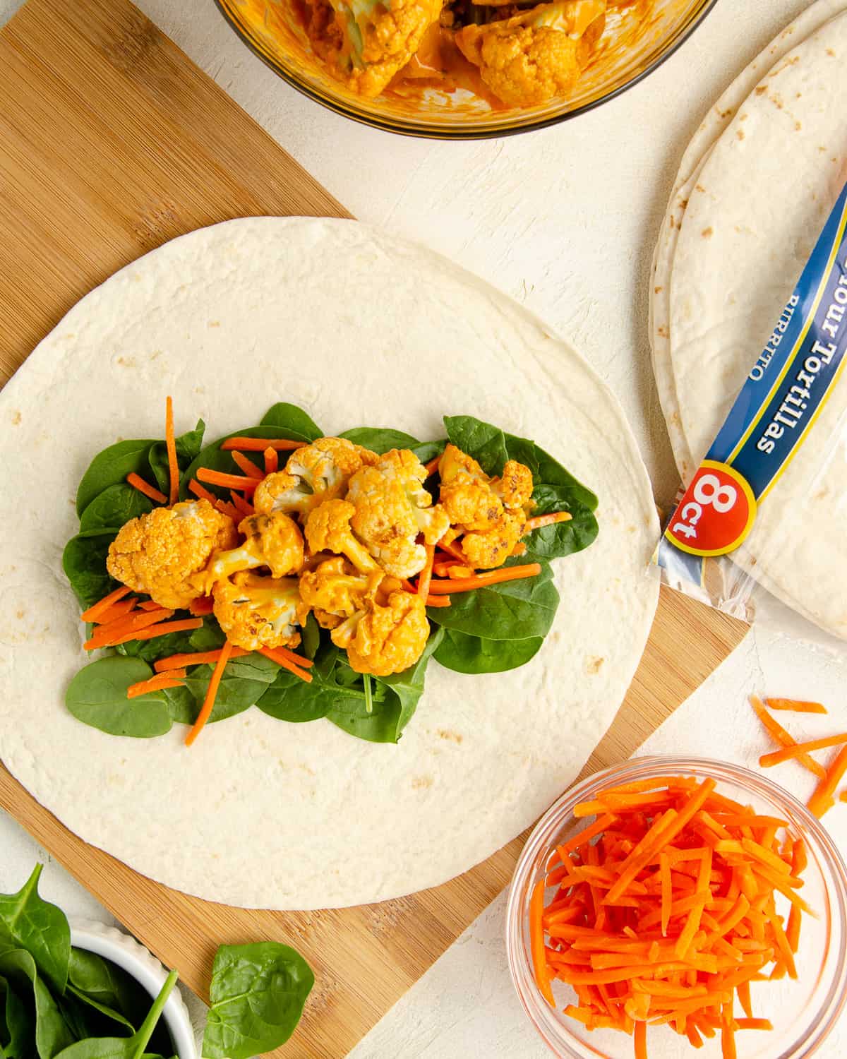 Step three of making the wrap: adding buffalo cauliflower on top of the carrots.