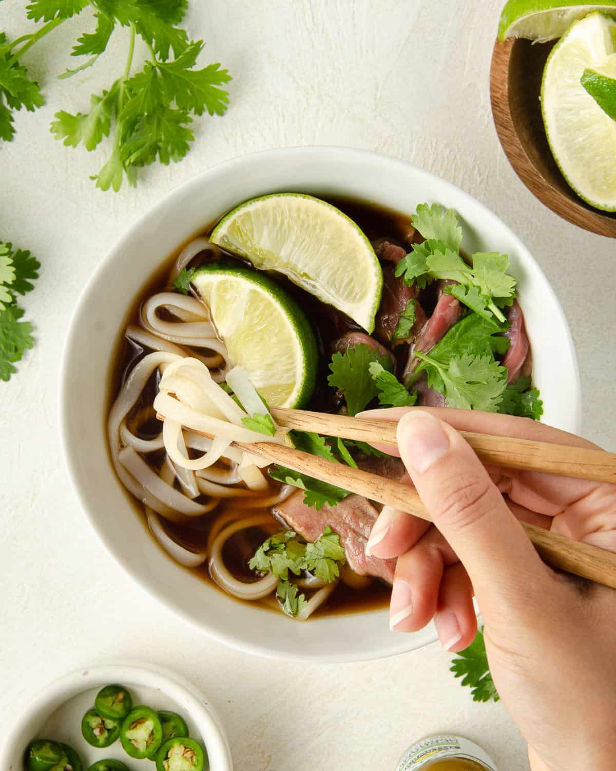 A hand holding chopsticks picking up a noodle from a bowl.